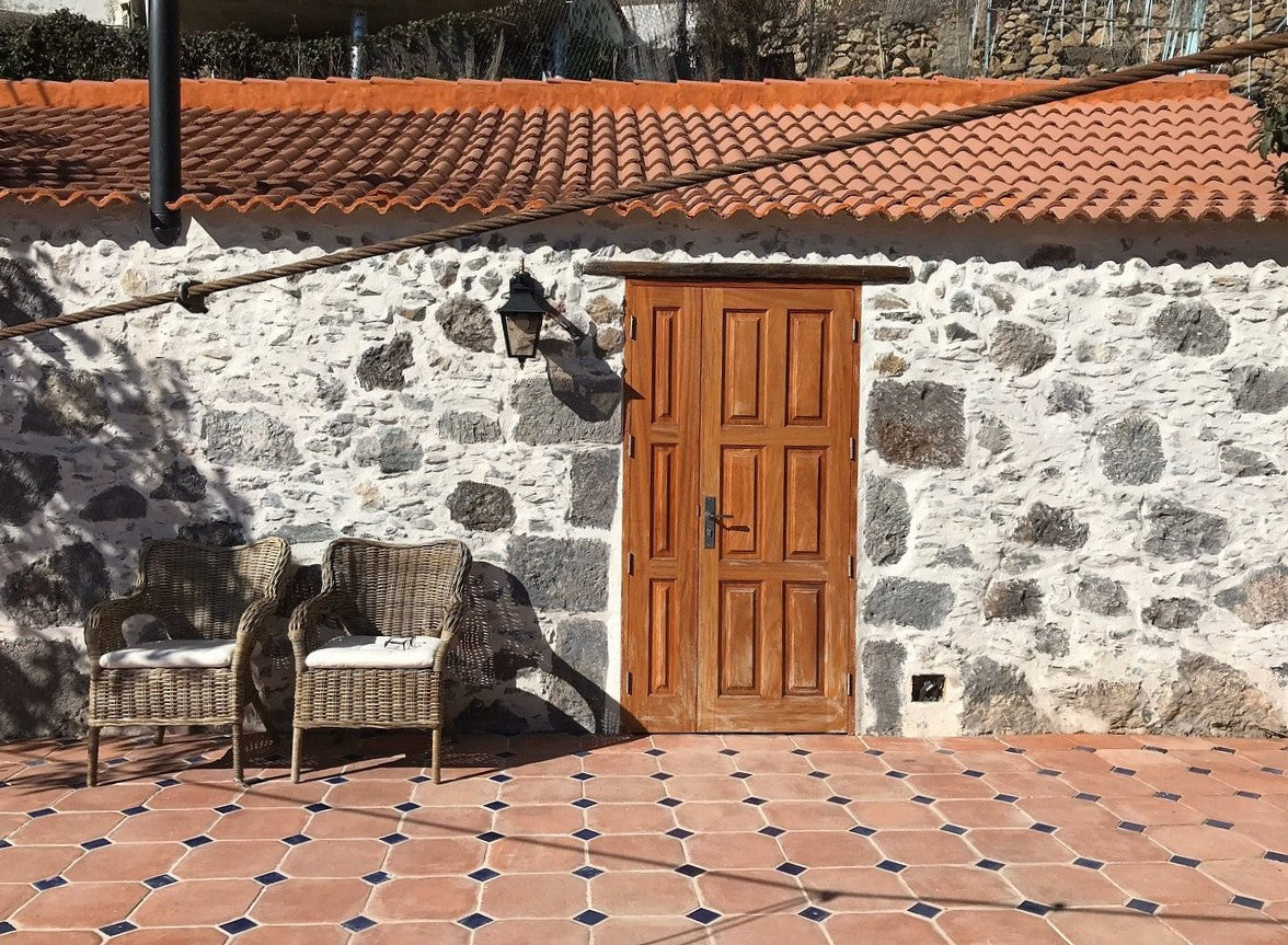 Stone wall with a wooden door and wicker chairs on a tiled patio